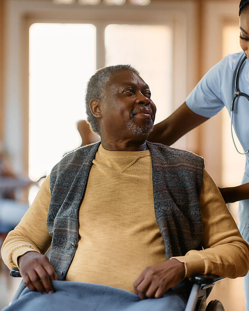 Elderly male in wheelchair with nurse assisting him